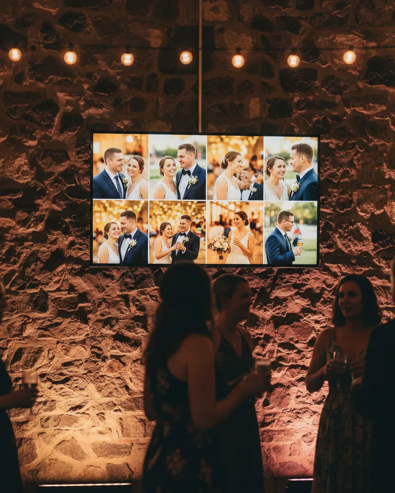 A large reception-hall TV playing a slideshow of event photos to a gathered crowd